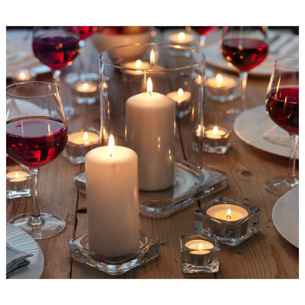 Ein Esstisch mit weißen Kerzen in klaren Glashaltern und Weingläsern mit Rotwein.