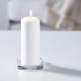 Eine brennende weiße Kerze in einem durchsichtigen Glashalter, die für Ambiente sorgt.
