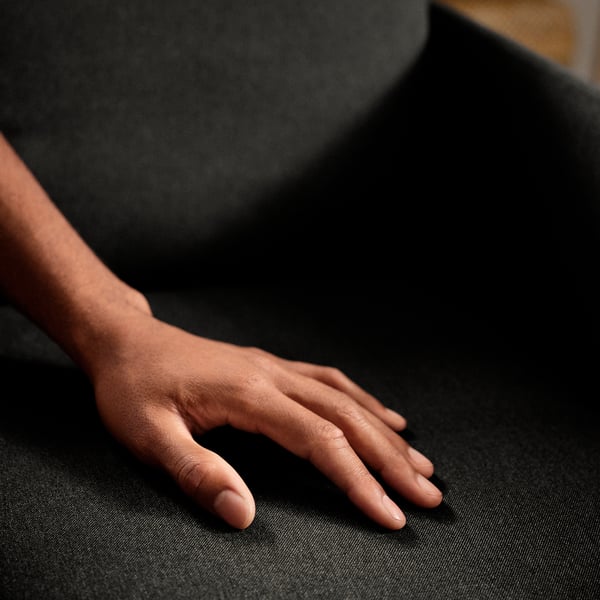 Die Hand ruht auf einem GLOSTAD-Sofa, das den weichen, strapazierfähigen Stoff zeigt. Einfach zu bewegen und zu montieren, auf Komfort und Stabilität ausgelegt.