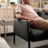 Ein Mann sitzt bequem auf einem modernen GLOSTAD-Sofa und präsentiert seine gepolsterten Armlehnen und Rückenkissen.