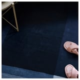 Dunkelblauer strukturierter Teppich mit hellblauen Streifen, rosa Pantoletten und weißem Stuhlbein.