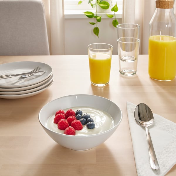 Tisch gedeckt mit Frühstücksartikeln: Schüsseln mit Joghurt mit Beeren, Säften und Tellern mit Besteck.