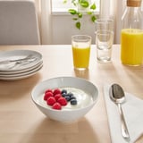Tisch gedeckt mit Frühstücksartikeln: Schüsseln mit Joghurt mit Beeren, Säften und Tellern mit Besteck.