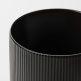 Schwarze Vase mit vertikalen Rillen auf weißem Hintergrund.