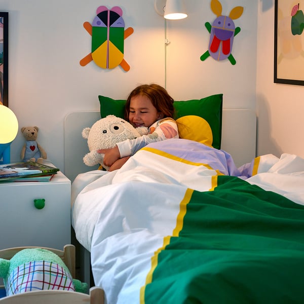 Kind schläft mit Spielzeug, buntes Bett, grünes Kissen, Bettdecke mit Insektenmotiven.