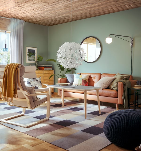 Modernes Wohnzimmer mit Ledersofa, Stuhl, Teppich, Spiegel, Lampe und grünen Wänden.