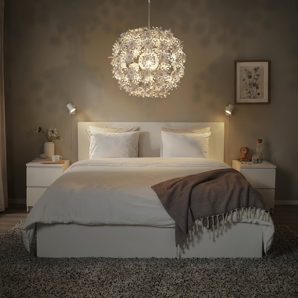 Modernes Schlafzimmer mit großer, kugelförmiger, weißer GRIMSÅS-Pendelleuchte mit Lichtmustern, weißem Bett, Nachttischen und grauer Decke.