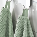 Zwei beige Handtücher hängen ordentlich an Haken, weich und flauschig, aus 100% Baumwolle, zur Verwendung ausgestellt.