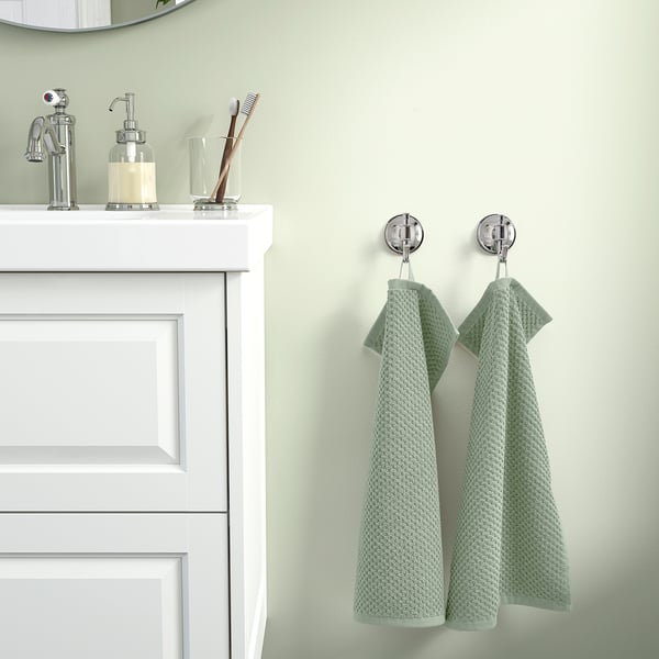 Modernes Badezimmer mit weißem Waschtisch, Chrom, 2 grünen Handtüchern und kleinem Dekor.