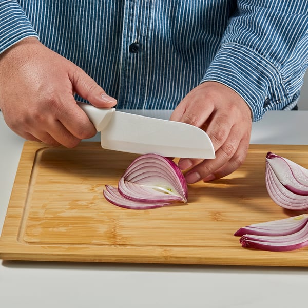 Die Person schneidet rote Zwiebel mit einem Keramikmesser auf einem hölzernen Schneidebrett in Scheiben. Zwiebeln werden teilweise gehackt, was die Schärfe der Messer zeigt.