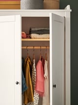 Weißer Holzschrank mit Kinderkleidung und Kleiderbügeln, ordentlich organisiert.