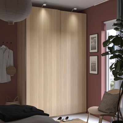Modernes Schlafzimmer mit HASVIK-Schranktüren aus hellem Holz, gestreiftem Hemdenbügel, Fenster, Schuhregal, Pflanzen und Stuhl.