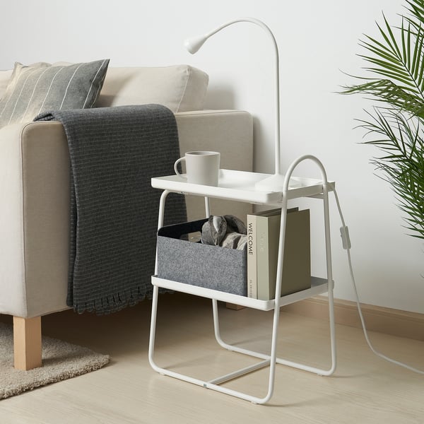 Gemütliches Wohnzimmer mit einem weißen HATTÅSEN-Beistelltisch, auf dem eine Tasse, Bücher und eine Lampe neben einem beigen Sofa stehen.