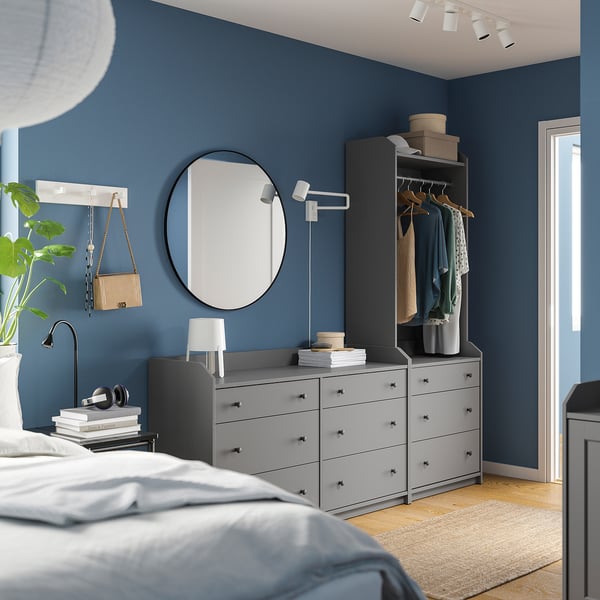 Modernes blaues Schlafzimmer mit grauen Schubladen und Kleiderschrank von HAUGA, rundem Spiegel, weißer Lampe, Pflanzen und Kopfhörern auf Büchern.