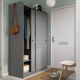 Moderner Eingangsbereich mit grauem HAUGA-Kleiderschrank, brauner Tasche, Turnschuhen und weißem Hocker auf einem Teppich.