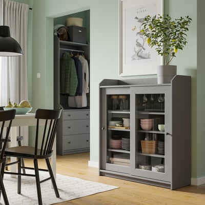 Modernes Esszimmer mit grauem HAUGA-Schrank mit Geschirr, schwarzen Stühlen und grünen Wänden.