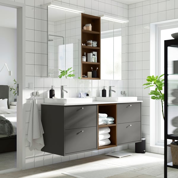 Moderner schwarzer Badezimmerwaschtisch mit zwei Waschbecken, offenen Regalen und eleganten Schränken. Großer Spiegel oben mit Handtüchern und Pflanze.