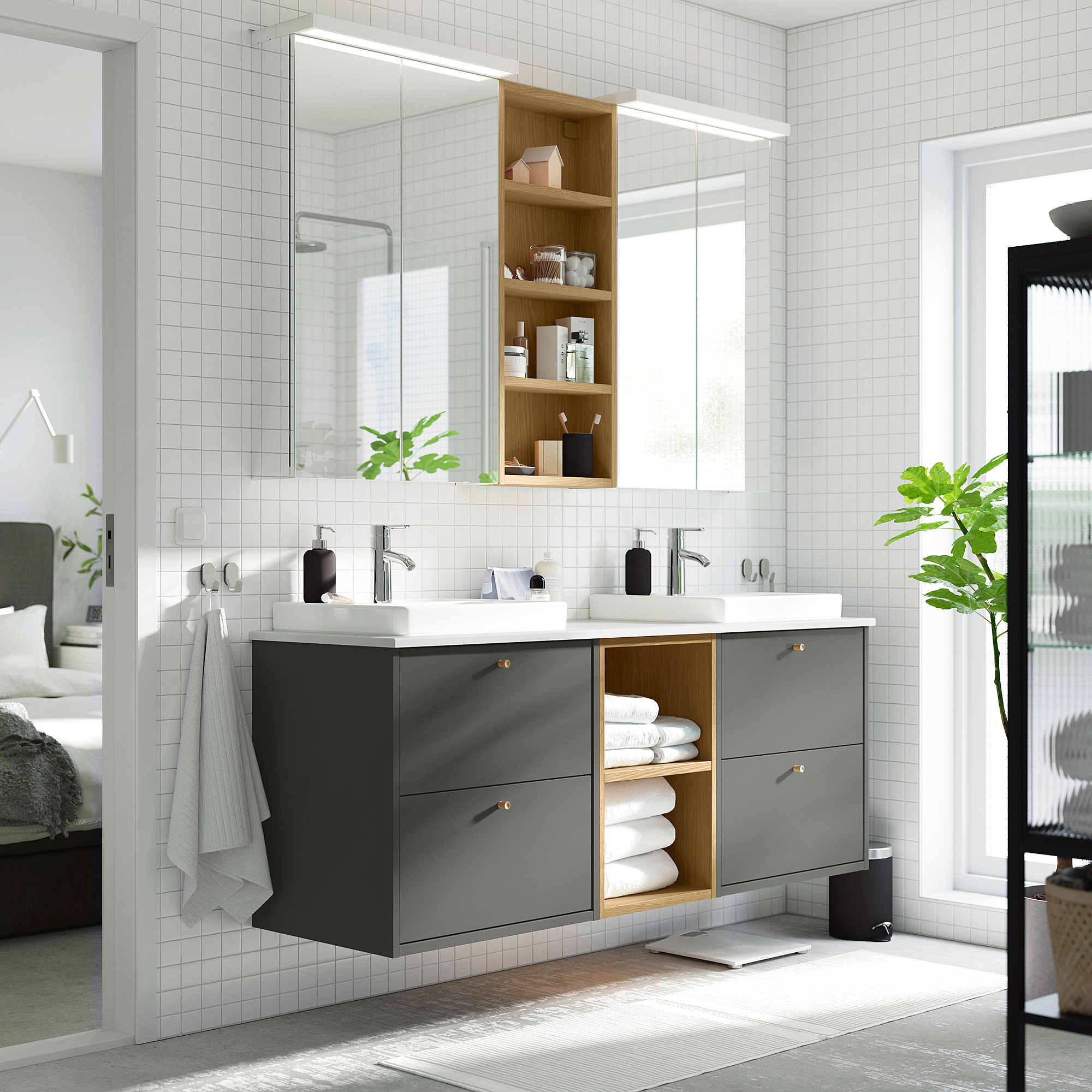 Modernes Badezimmer mit dunkelgrauem Doppelwaschtisch von HAVBÄCK, weißer Arbeitsplatte und großem Spiegel. Handtücher hingen neben dem offenen Regal.