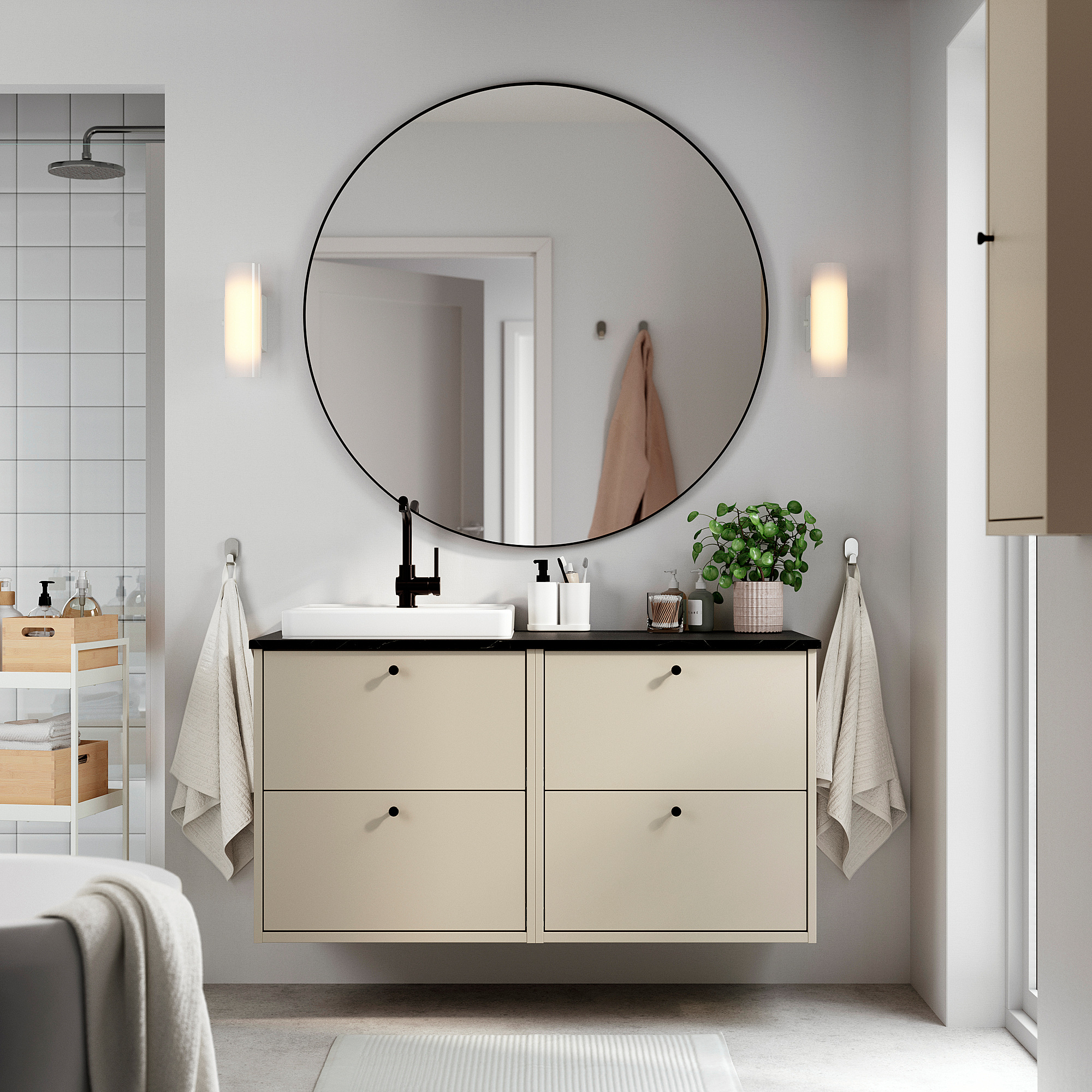 Modernes Badezimmer mit beigem HAVBÄCK-Waschtisch, rundem Spiegel, weißen Handtüchern und Pflanzen.