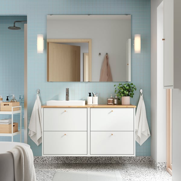 Modernes Badezimmer mit weißem Waschtisch, großem Spiegel und viel Stauraum. Zwei Lichter und eine Pflanze werten die Einrichtung auf.