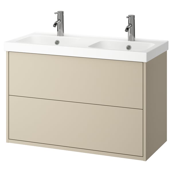 Ein cremefarbener Waschtisch mit zwei Waschbecken und zwei Schubladen. Der Waschtisch hat ein schlankes, modernes Design mit verchromten Armaturen und Knöpfen.