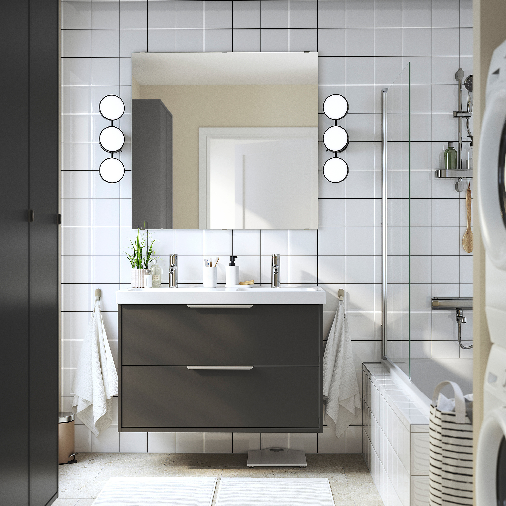 Modernes Badezimmer mit schwarzem HAVBÄCK-Waschtisch, weißem Doppelwaschbecken, grauen Fliesen und runden Spiegeln. Weiße Handtücher, schwarzer Waschtrockner.