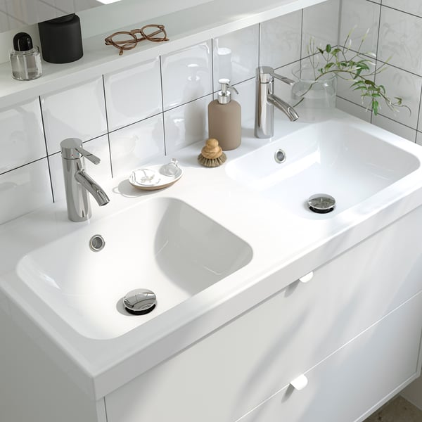 Sauberes, modernes Waschbecken mit zwei Wasserhähnen, Seifenspender und Pflanzen.