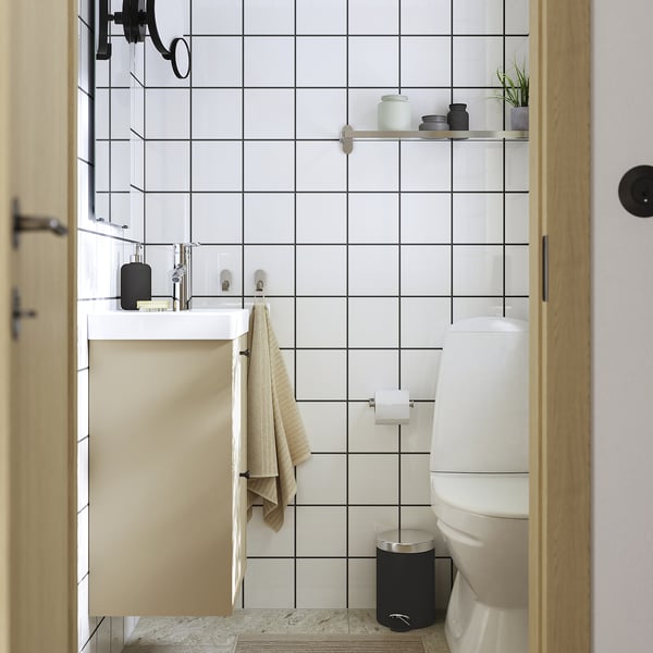 Ein minimalistisches Badezimmer mit weißen Gitterfliesen, einem mattbeigen Schrank, einem weißen Waschbecken und einer weißen Toilette sowie einer Glastür.