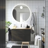 Modernes Badezimmer mit Spiegel, grauem Schrank, heller Holztheke, weißem Waschbecken, grauen Fliesen, Glasdusche und Handtüchern.
