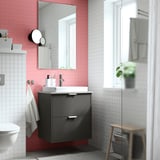 Modernes Badezimmer mit dunkelgrauen HAVBÄCK-Möbeln, weißem Waschbecken, Spiegel, WC, Fenster und Holzhocker mit Pflanze.
