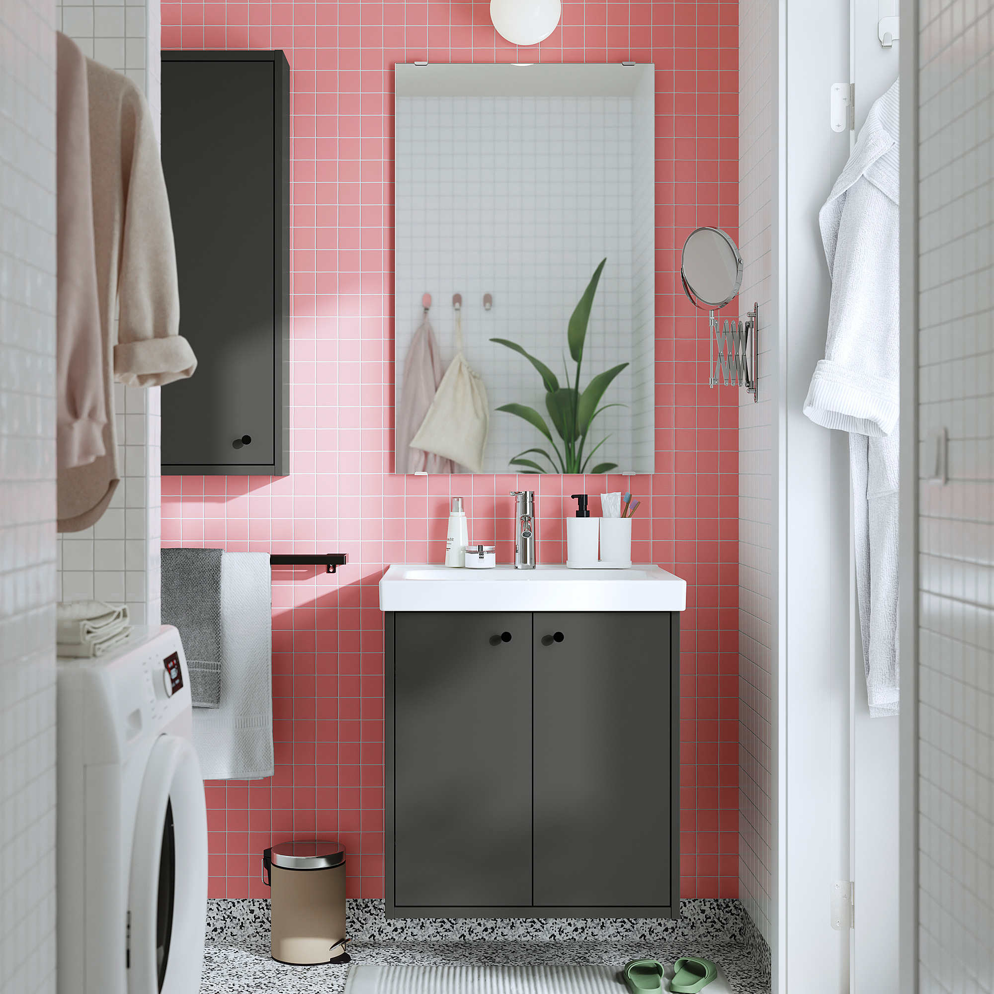 Kleines, modernes Badezimmer mit rosa Fliesen, dunkelgrauem Schrank, weißem Waschbecken, Spiegel und Waschmaschine in schlichtem Design.