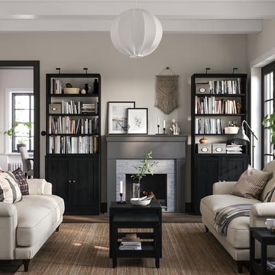 Modernes Wohnzimmer mit schwarzem HAVSTA-Bücherregal, cremefarbenen Sofas, grauem Teppich und Kamin.