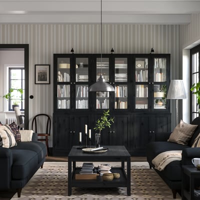 Wohnzimmer mit schwarzen HAVSTA-Bücherregalen, dunkelblauem Sofa, gemustertem Teppich und gestreiften Tapeten.