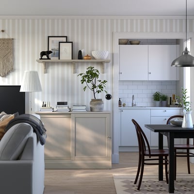 Moderner Wohnbereich mit weiß gestreiften Wänden, einem grauen Sofa, einem Esstisch aus Holz und einem Sideboard aus Metall mit Holzschubladen.