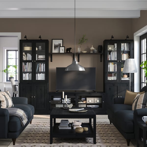 Modernes Wohnzimmer mit dunklen Holzmöbeln, Flachbildfernseher, Bücherregalen und gemütlichen Sitzgelegenheiten. Gestylt mit einer Lampe und Dekor.
