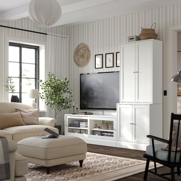 Modernes Wohnzimmer mit weißen HAVSTA-Aufbewahrungseinheiten, beigem Sofa, gemustertem Teppich und gestreifter Tapete; Fernseher und Dekorationsartikel werden ausgestellt.