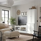 Modernes Wohnzimmer mit weißen HAVSTA-Aufbewahrungseinheiten, beigem Sofa, gemustertem Teppich und gestreifter Tapete; Fernseher und Dekorationsartikel werden ausgestellt.