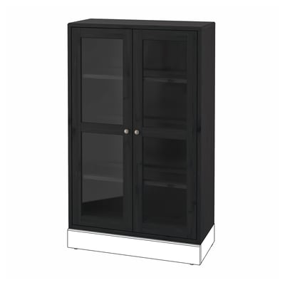 Ein schwarzer HAVSTA-Schrank mit Glastüren aus Kiefernholz, der auf einem weißen Sockel steht.