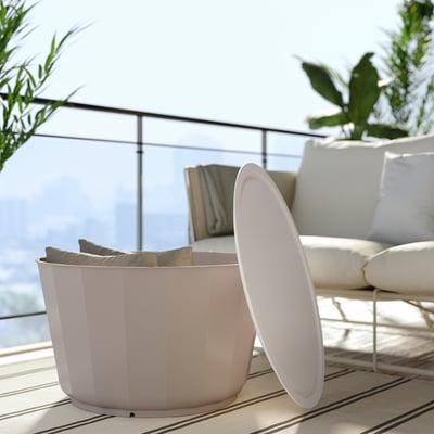 Minimalistische Umgebung im Freien mit beigem Sofa, weißem Mülleimer, Glasgeländer und Grün.