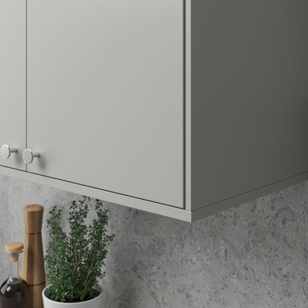 Moderner Küchenschrank mit elegantem grauem Finish und runden Griffen, darunter eine Topfpflanze und ein Holzmahlwerk.