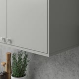 Moderner Küchenschrank mit elegantem grauem Finish und runden Griffen, darunter eine Topfpflanze und ein Holzmahlwerk.