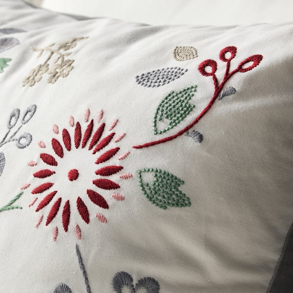 Besticktes Kissen mit leuchtend roten und grünen Blumenmustern auf cremefarbenem Stoff, das hochwertige Nähte und Handwerkskunst zeigt.
