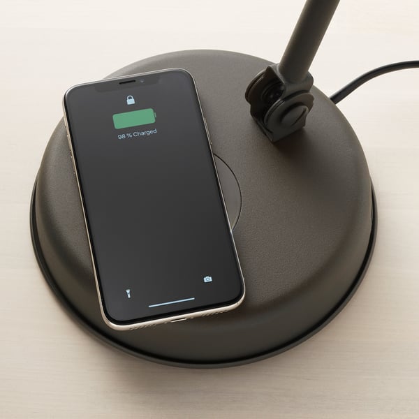 Ein Smartphone zeigt 98 % Ladung auf einem kabellosen Ladepad an, das in eine Lampe im Vintage-Stil integriert ist.