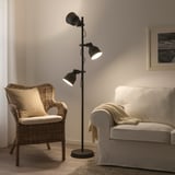 HEKTAR Stehleuchte, schwarz, Industriedesign, große Metallschirme, höhenverstellbar, steht hoch neben Korbstuhl und beigem Sofa.