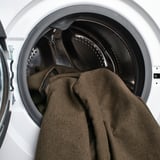 Offene Waschmaschine mit grauer Hose innen, bereit zum Waschen.