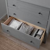 Die offene Kommodenschublade aus grauem Holz zeigt ordentlich gefaltete Kleidung und Socken, mit leichtgängigem Mechanismus und Wandverankerungsbeschlägen.