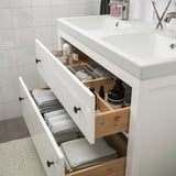 Weißer Badezimmerschrank mit offenen Schubladen, in dem Handtücher und Toilettenartikel organisiert sind.