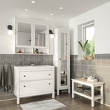 Modernes weißes Badezimmer mit HEMNES-Waschtisch, breitem Spiegelschrank, hohem Stauraum und Bank. Dunkelgraue Fliesen, ovale Becken und runde Leuchten.