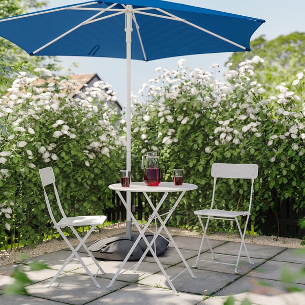 Garten mit weißem Tisch, Stühlen, blauem Sonnenschirm und weißen Blumen.