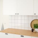 Eine moderne Küche mit einer Holzarbeitsplatte, einer weiß gefliesten Rückwand, hängenden Handtüchern und Topfkräutern, die einen funktionalen und organisierten Raum demonstrieren.